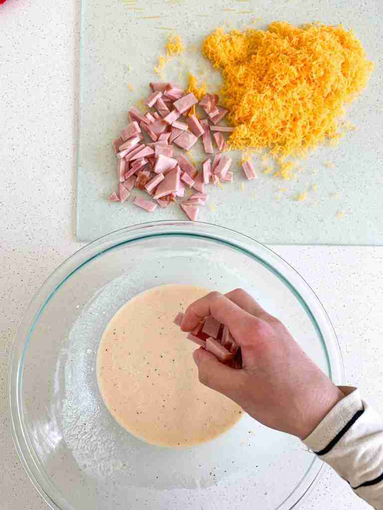 hand adding ham slices into the custard mixture