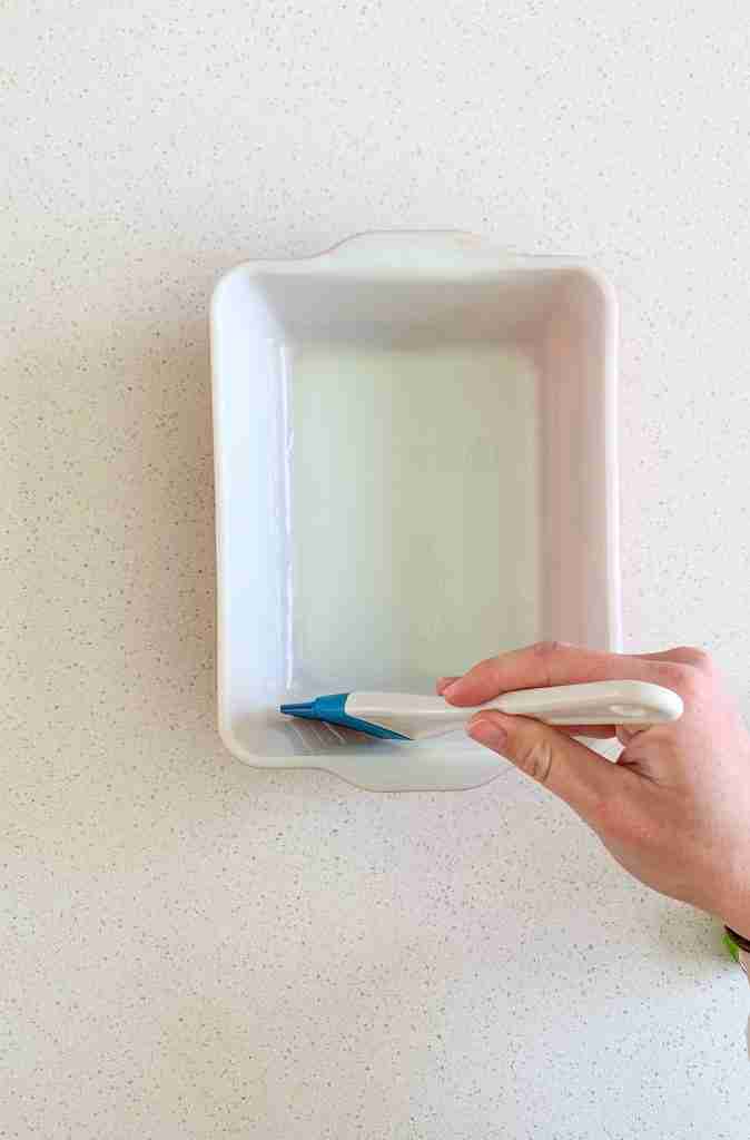 hand greasing a casserole dish 