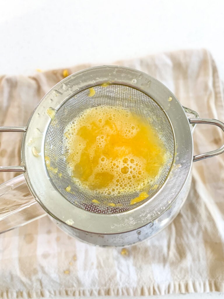 straining fresh orange juice through strainer into pitcher
