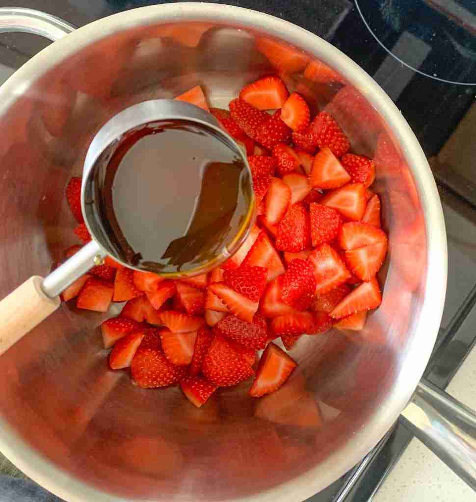 adding honey to strawberries in a pan