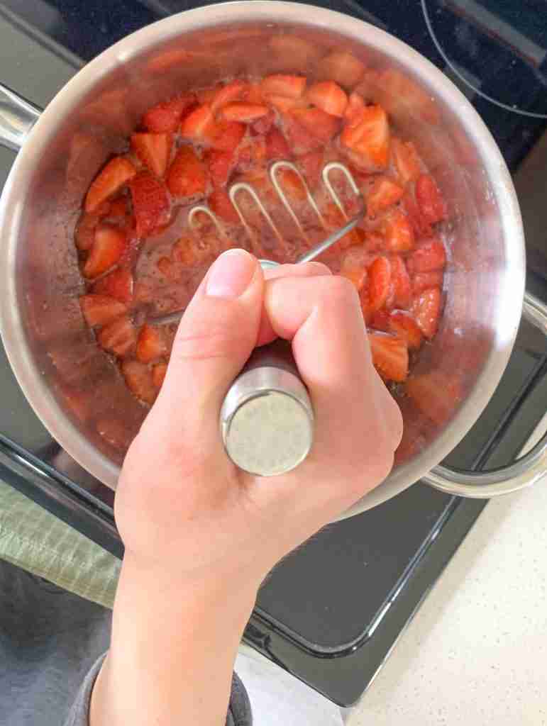 masher mashing strawberries in a pot