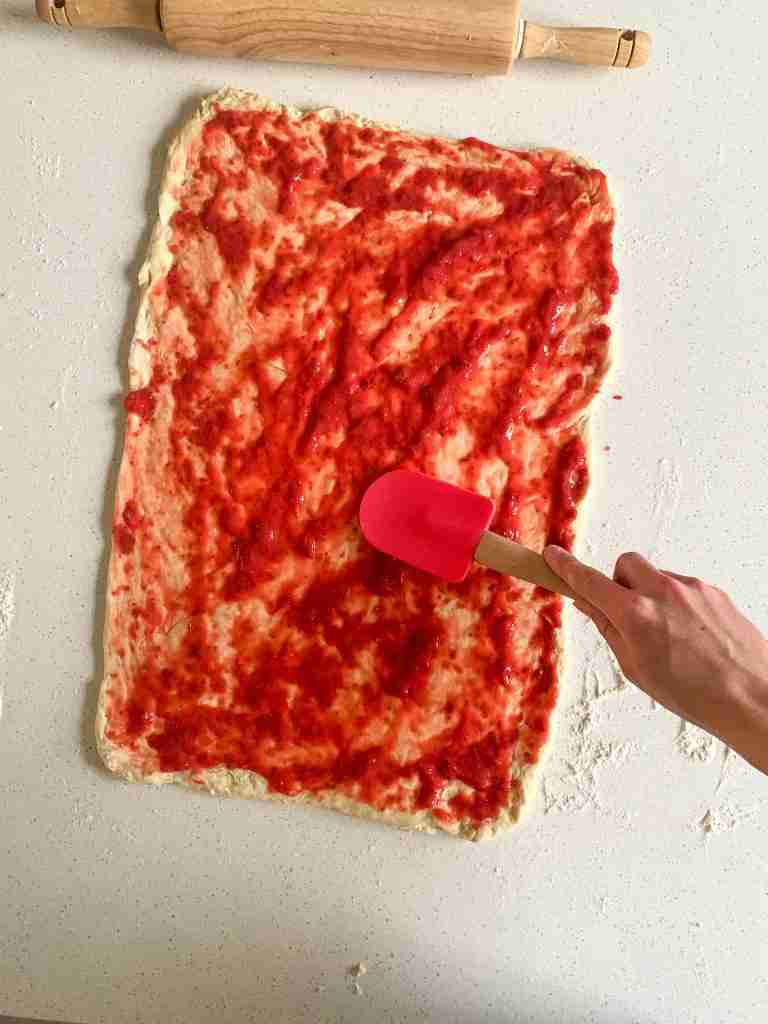 hand spreading jam on dough