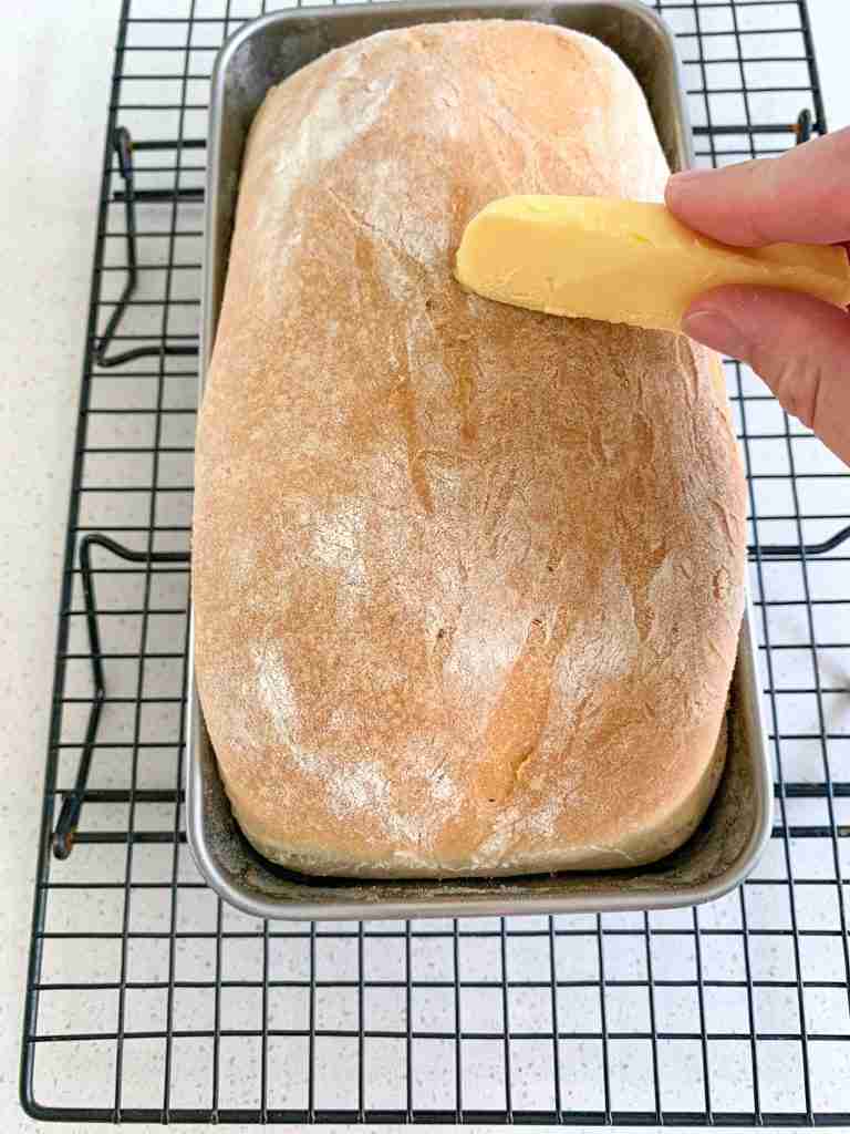 hand brushing butter on bread loaf