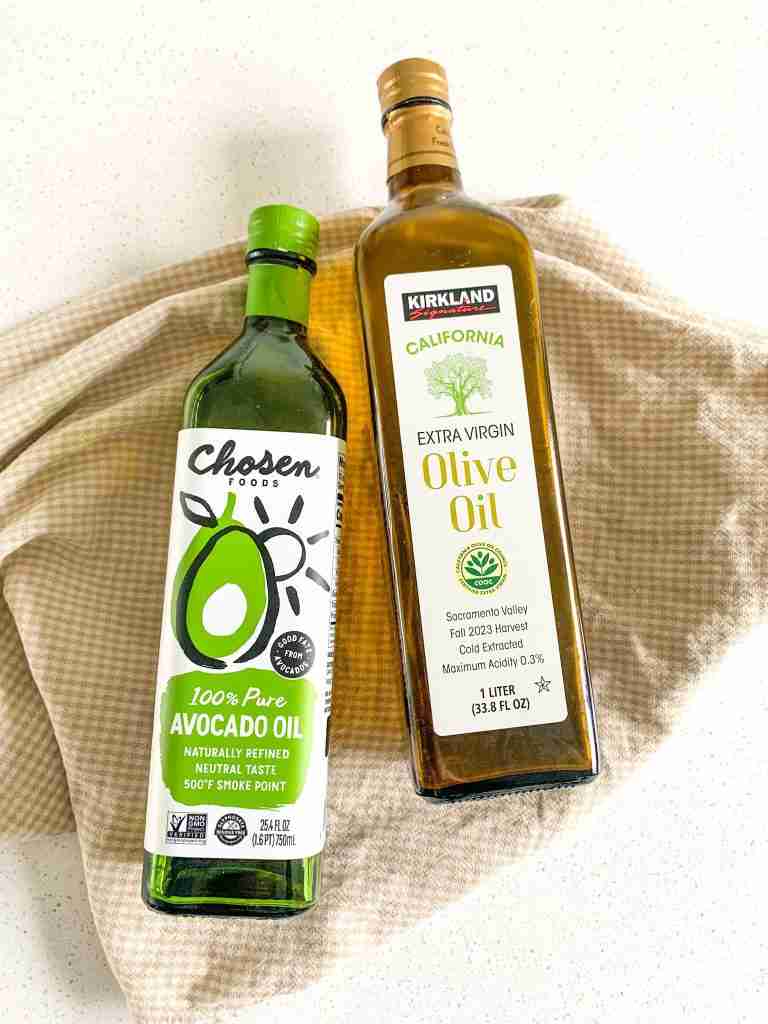 bottle of olive oil and bottle of avocado oil laying on a towel on the counter