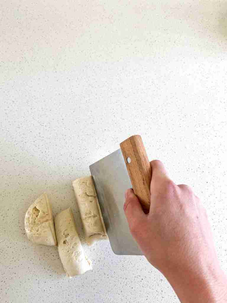 hand using a bench scraper to cut dough into 6 pieces