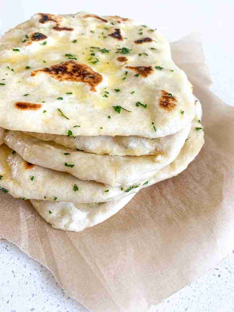 stack of flattened breads brushed with herbs on parchment paper