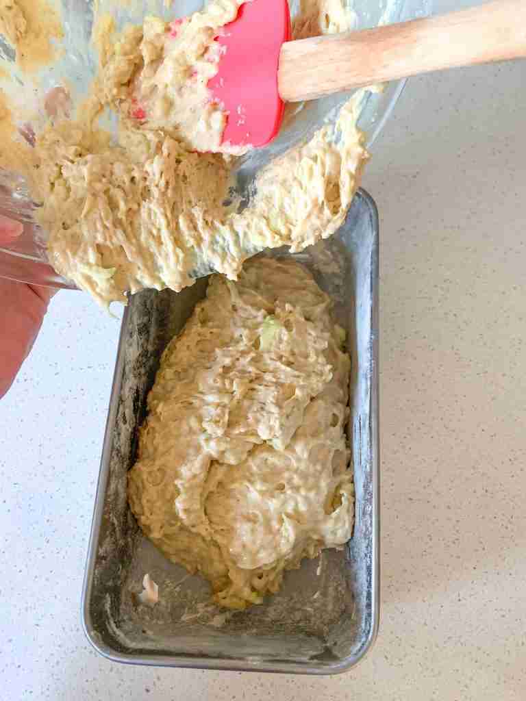 hands pouring batter into a loaf pan