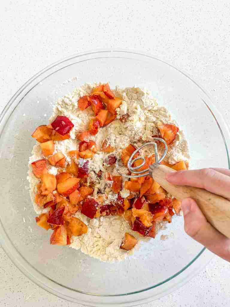 adding in peach chunks to dry ingredients and stirring to combine