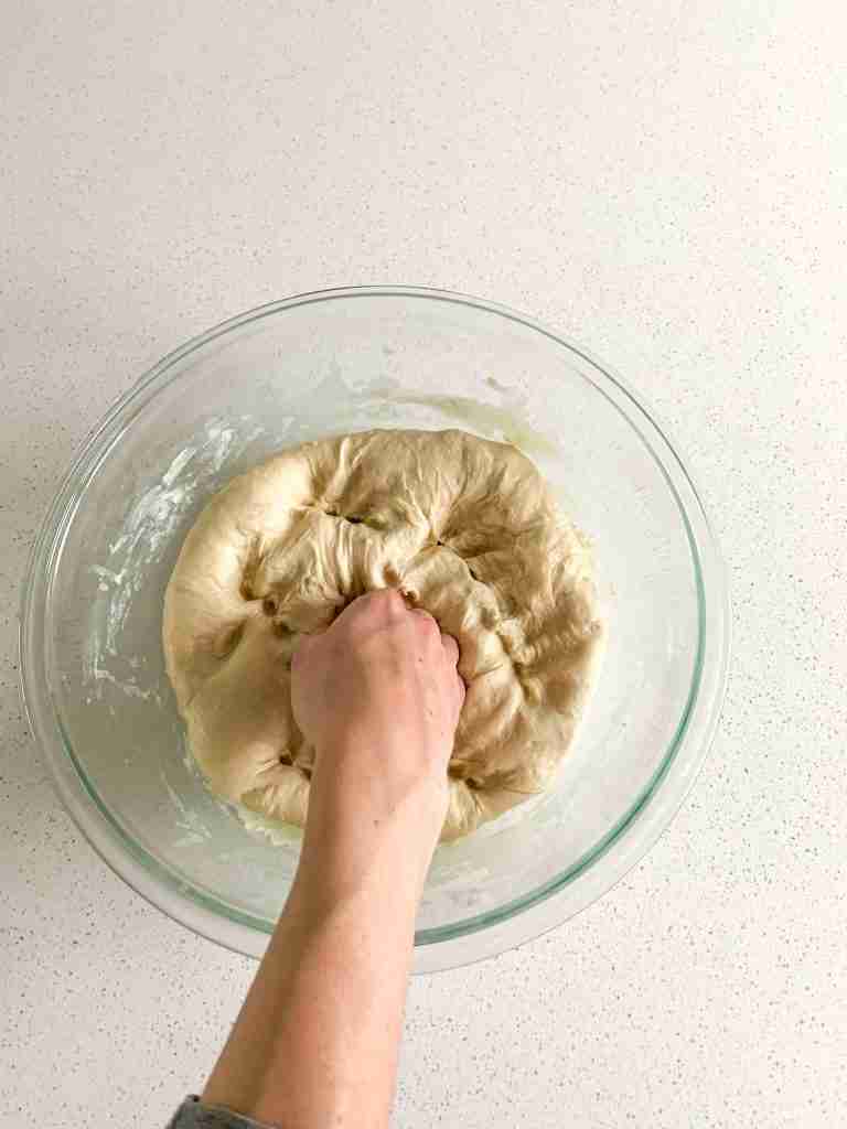 hand punching down dough in a bowl to get out gas bubbles