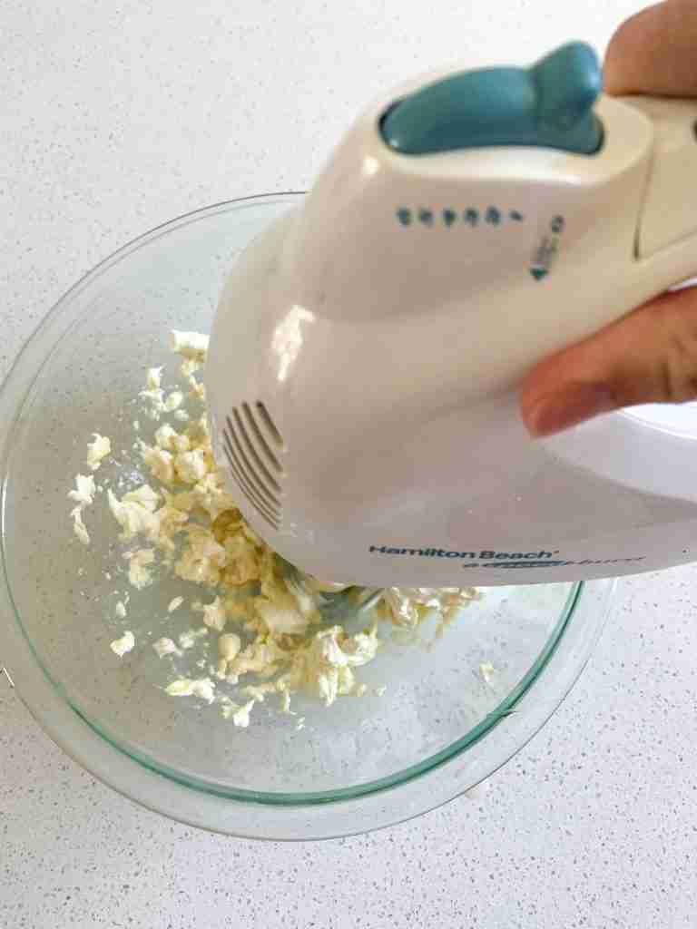 hand using a mixer to combine cream cheese frosting