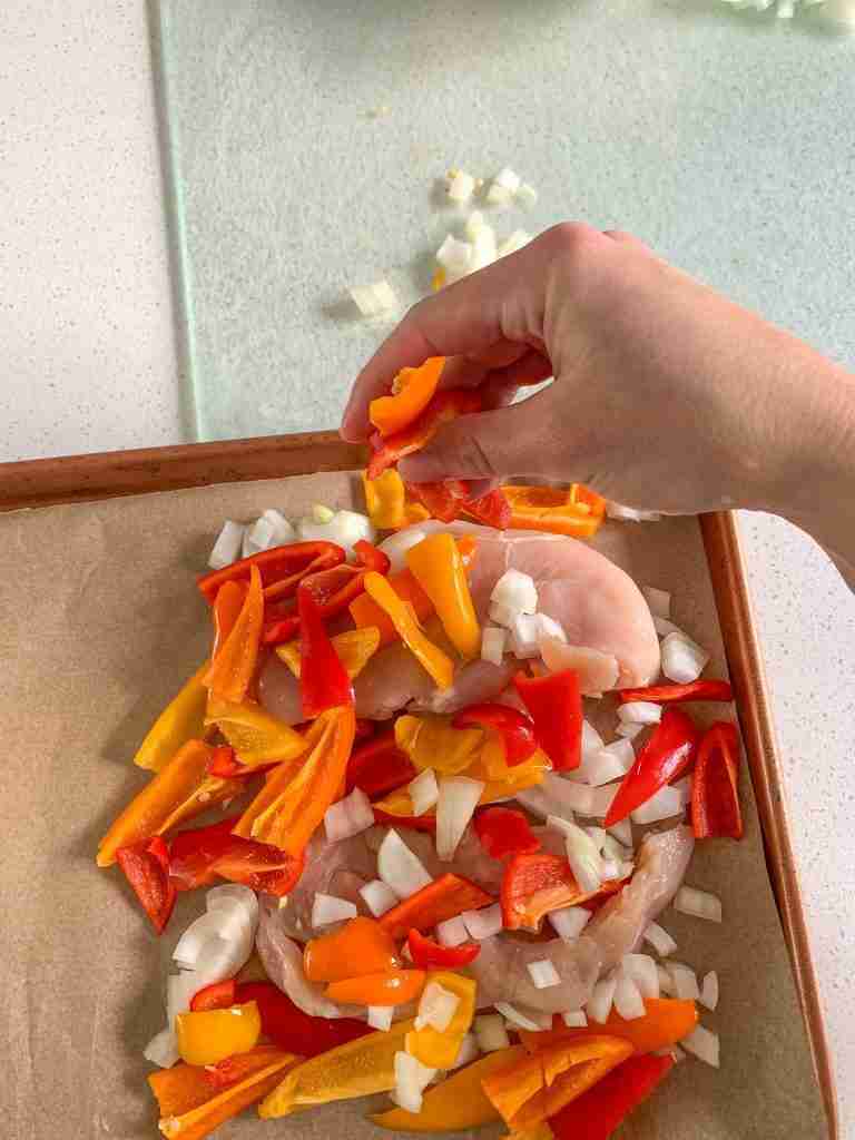 hand moving chicken peppers and onion slices onto a sheet pan