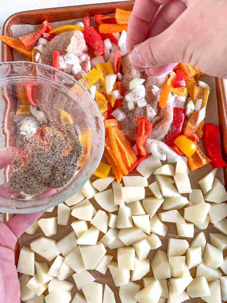 hands seasoning chicken and peppers with spice mix