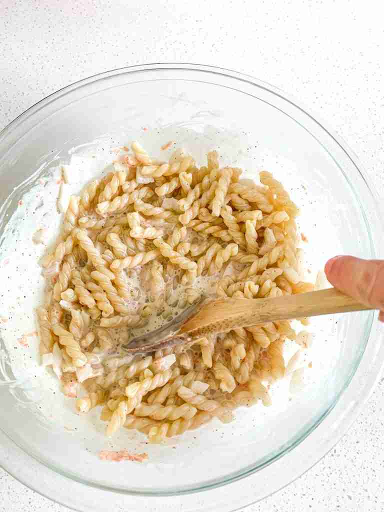 hand stirring pasta into a mayo mixture