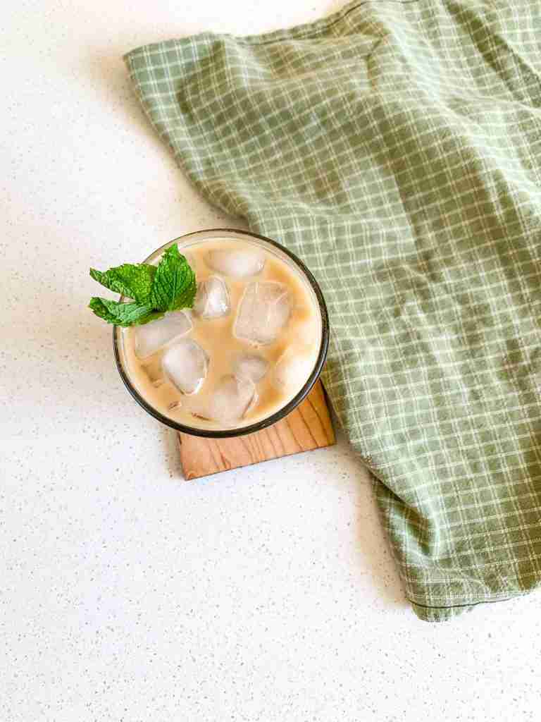 cup of iced coffee on a wooden coaster with a green towel by it