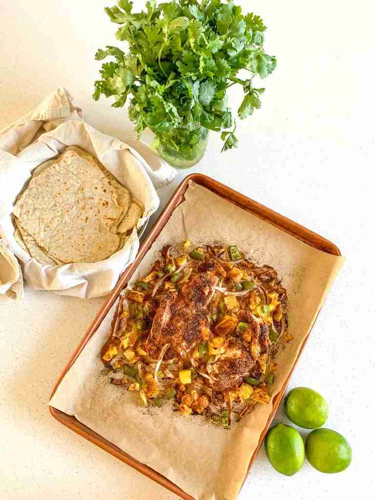 chicken breast and veggies on a sheet pan with taco shells, limes, and cilantro