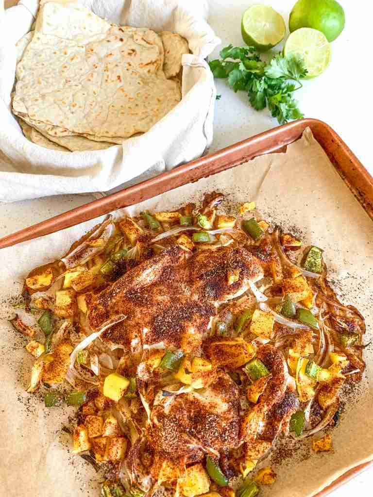 chicken breast and veggies on a sheet pan with taco shells, limes, and cilantro
