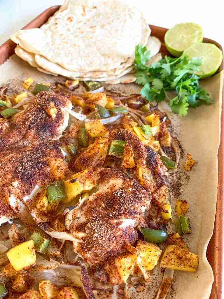 chicken breast and veggies on a sheet pan with taco shells, limes, and cilantro