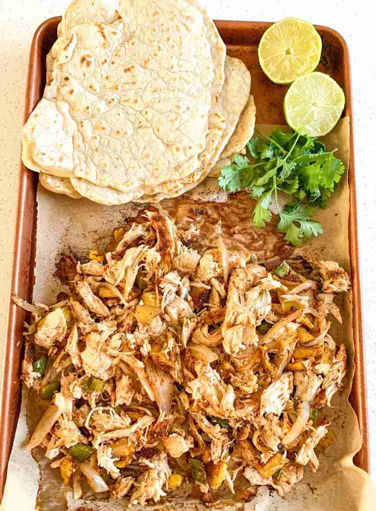 shredded chicken on a sheet pan with taco shells, limes, and cilantro