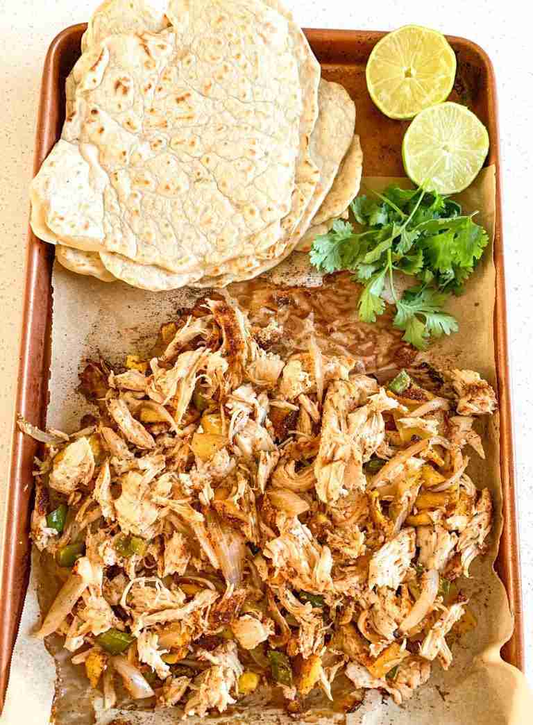 shredded chicken on a sheet pan with taco shells, limes, and cilantro