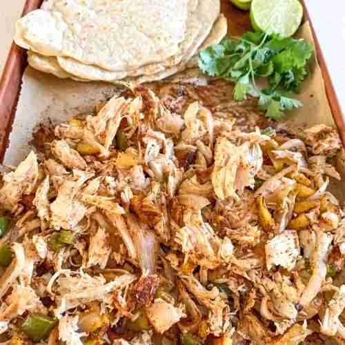 shredded chicken on a sheet pan with taco shells, limes, and cilantro