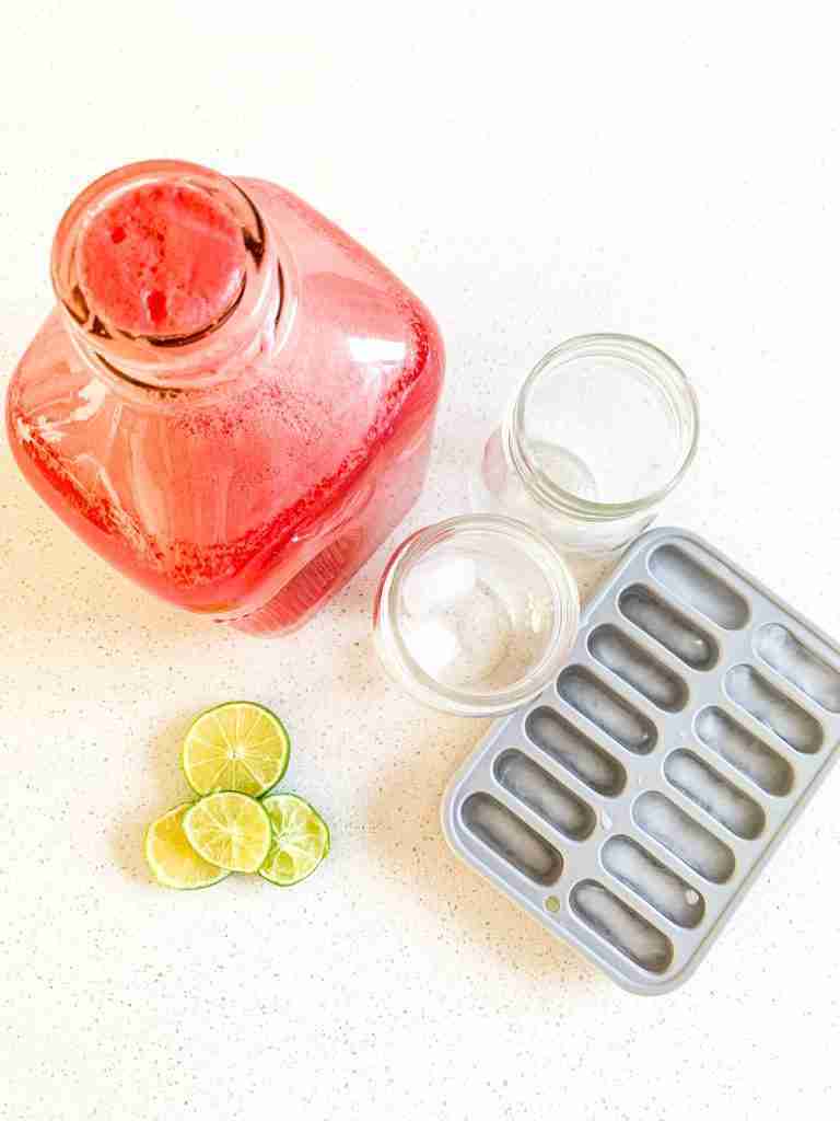 jug of watermelon drink iced cubes lime slices and glasses on a counter