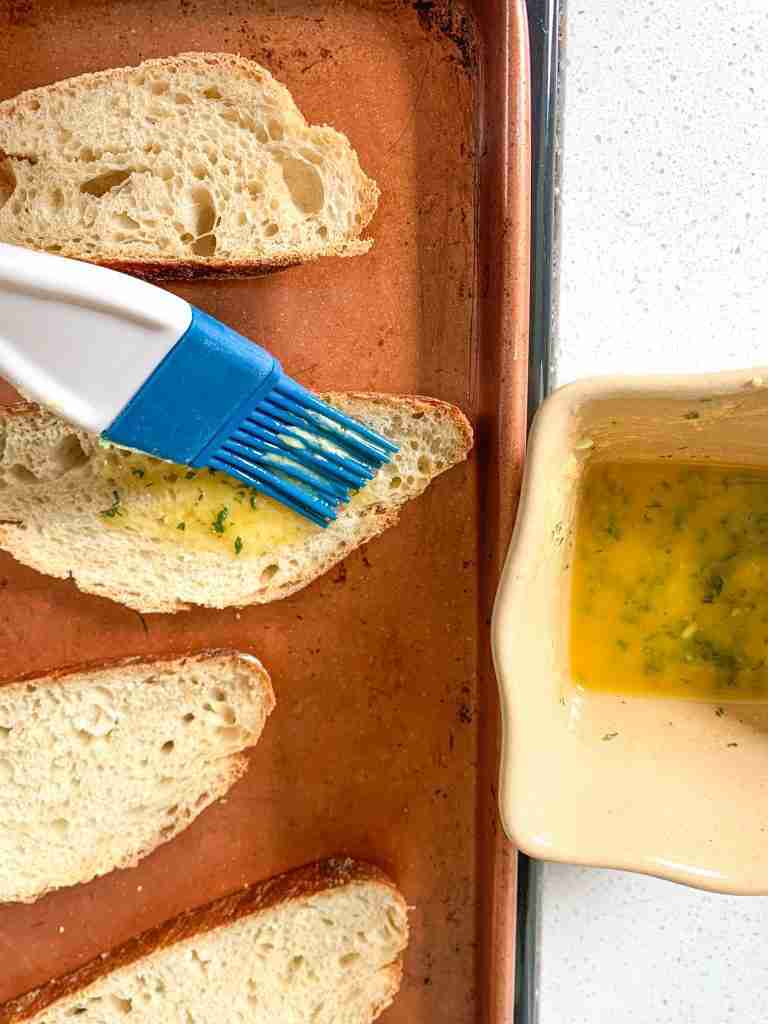 garlic butter being brushed on to bread slices