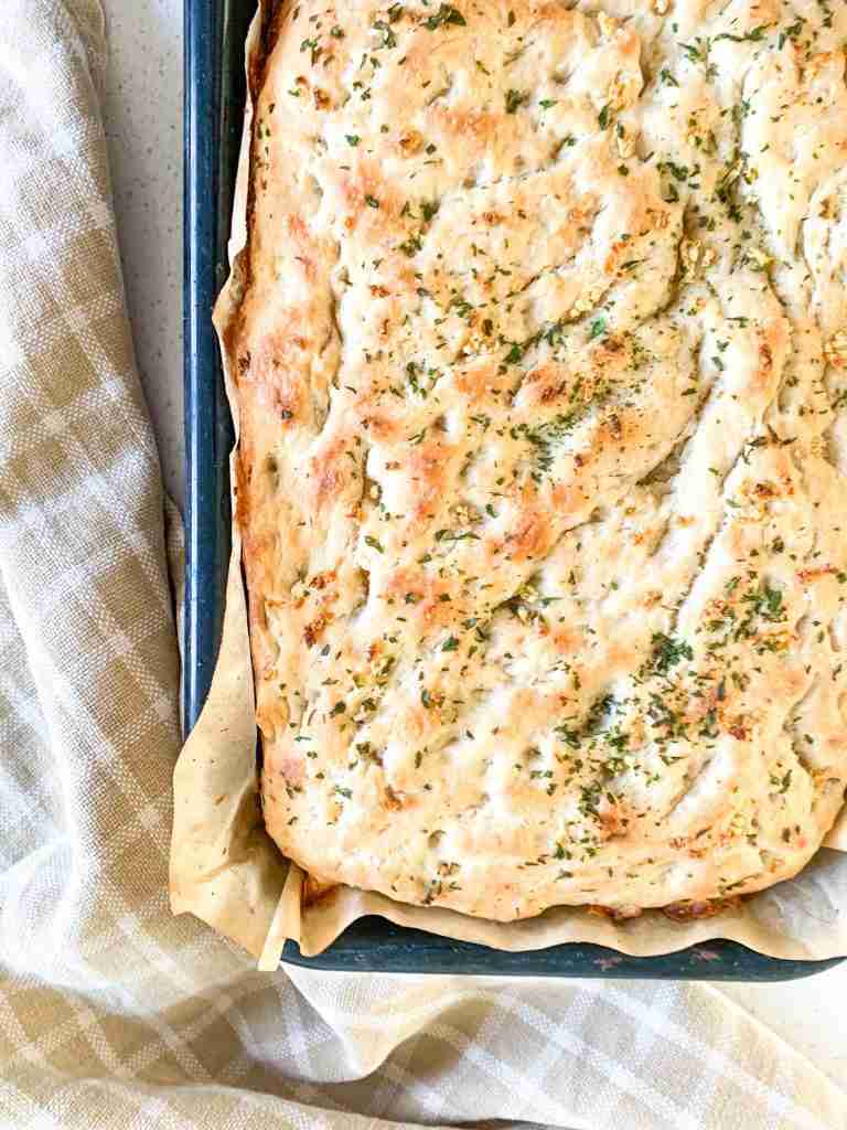 focaccia bread in a pan with a towel beside it