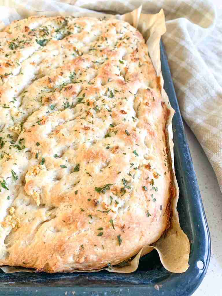 focaccia bread in a pan with a towel beside it