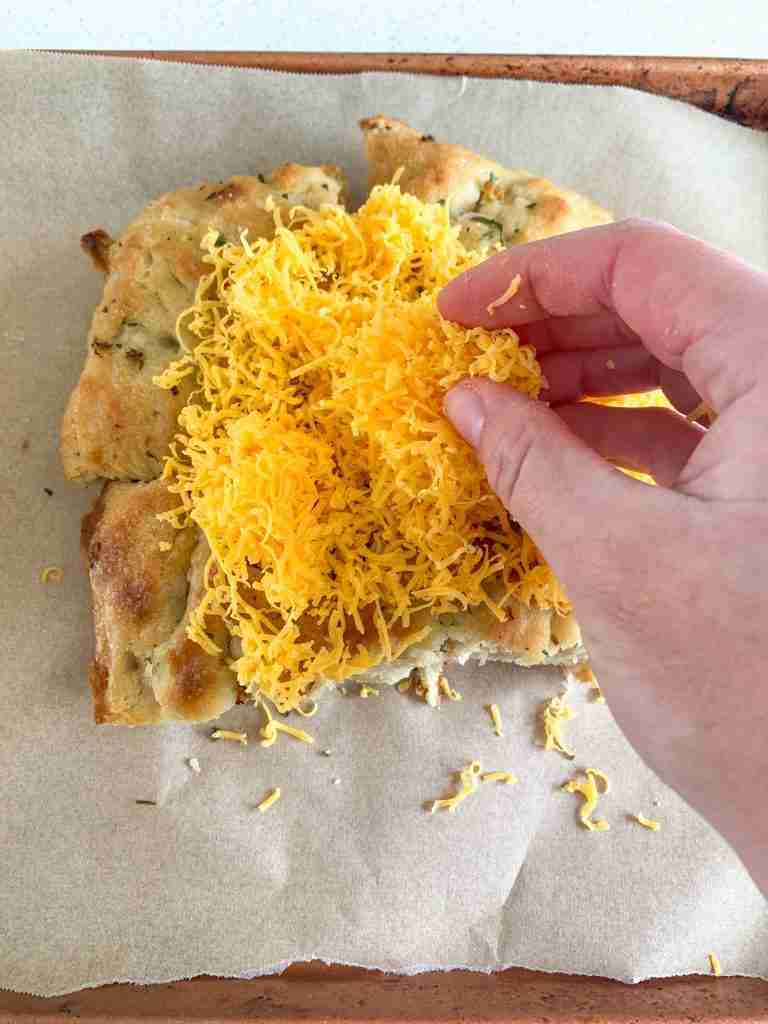 hand putting cheese on a focaccia bread slice