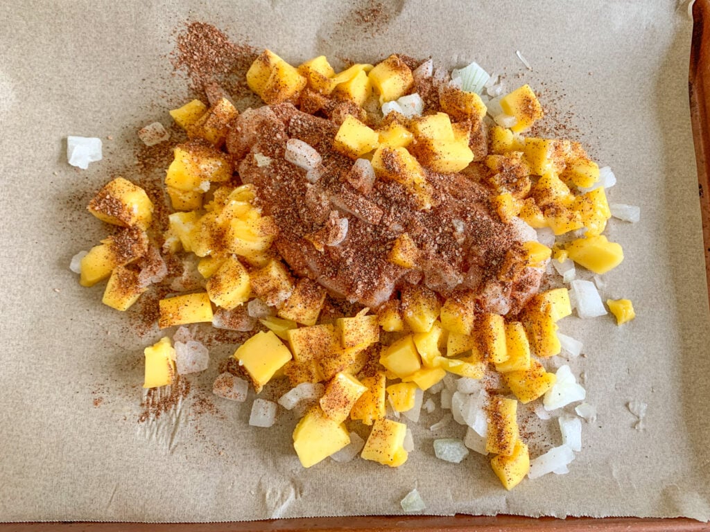 chicken, onion, and mangos seasoned on the sheet pan