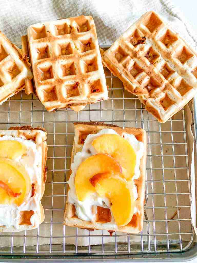 freshly made sourdough peach waffles topped with whipped cream and peaches