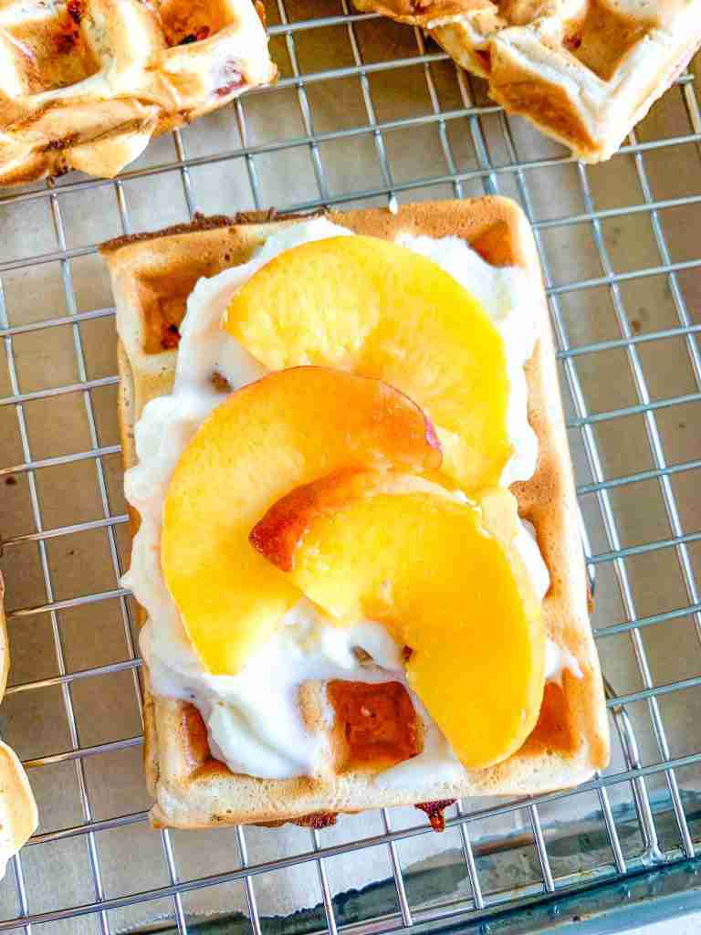 freshly made sourdough peach waffles topped with whipped cream and peaches