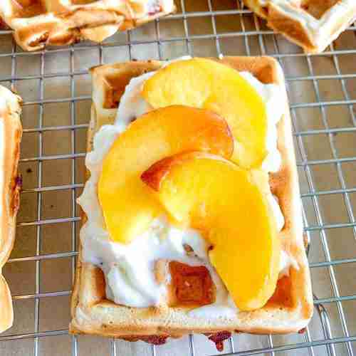 freshly made sourdough peach waffles topped with whipped cream and peaches
