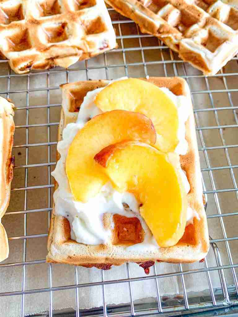 freshly made sourdough peach waffles topped with whipped cream and peaches
