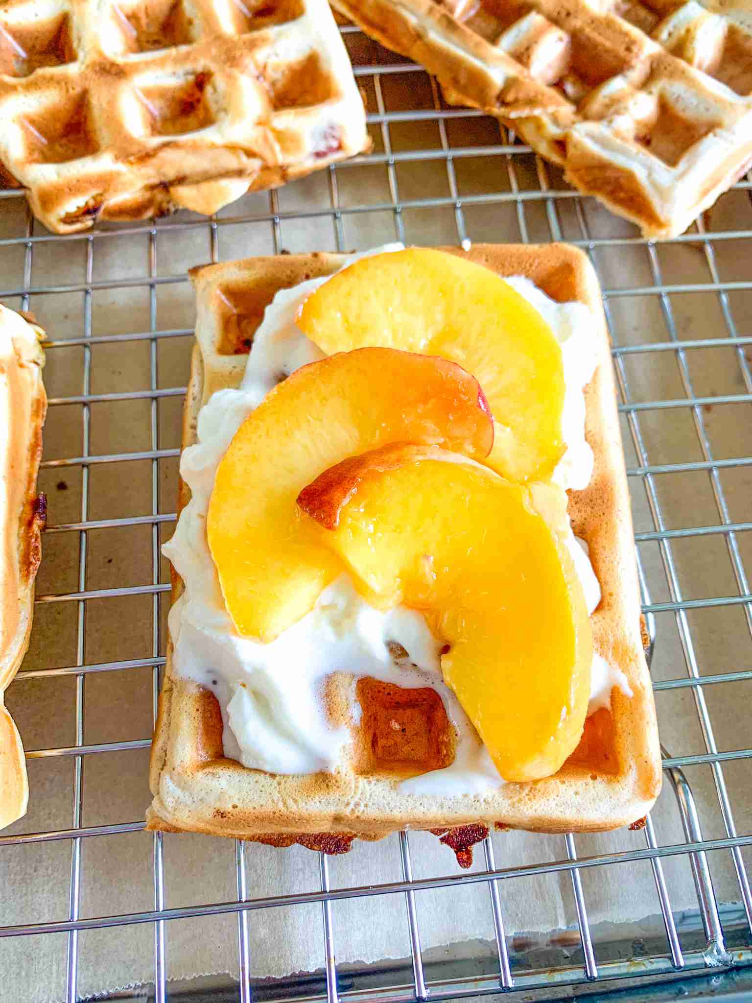 freshly made sourdough peach waffles topped with whipped cream and peaches