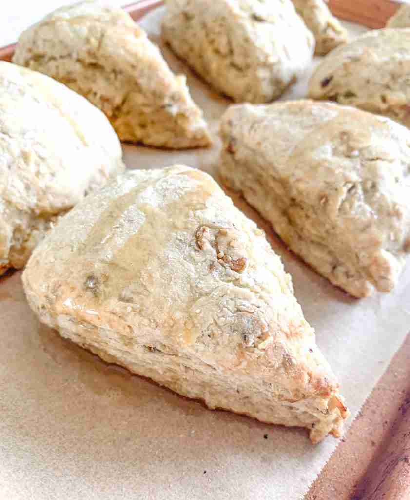 baked sourdough scones sitting on a sheet pan drizzled with maple syrup