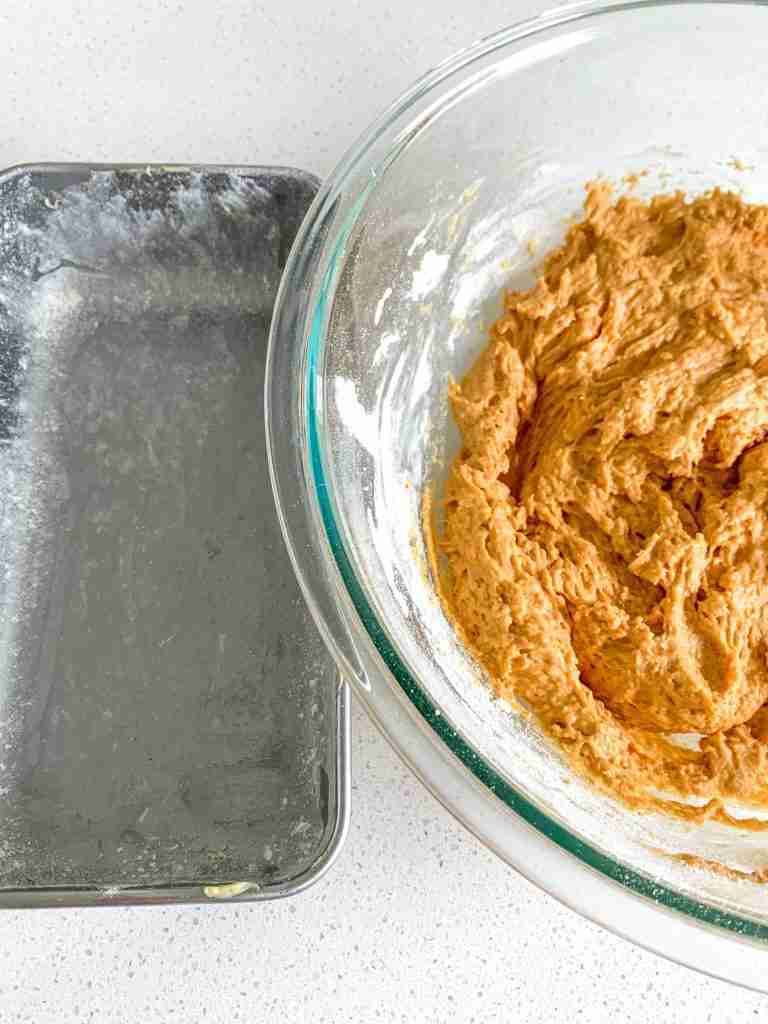 bowl of pumpkin bread batter and a prepared loaf pan beside it