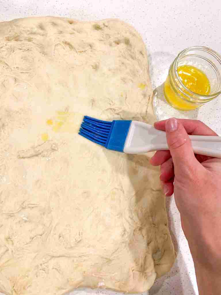 brushing butter onto rolled out bread dough