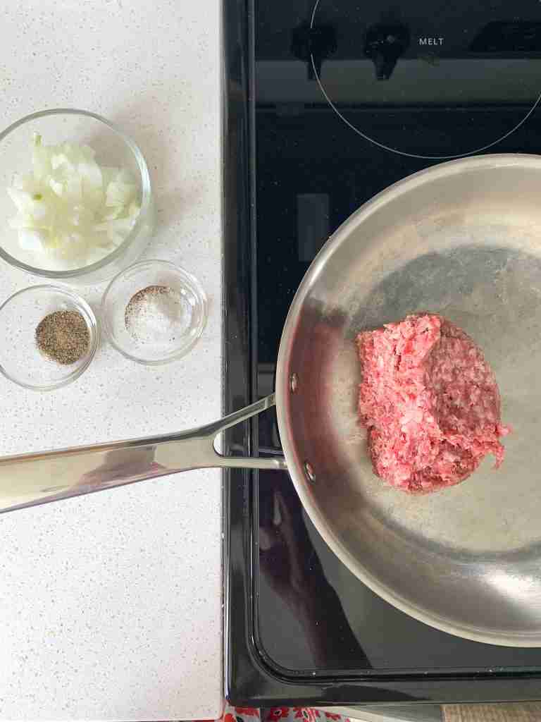ground beef in a skillet on the stovetop with other ingredients sitting beside it