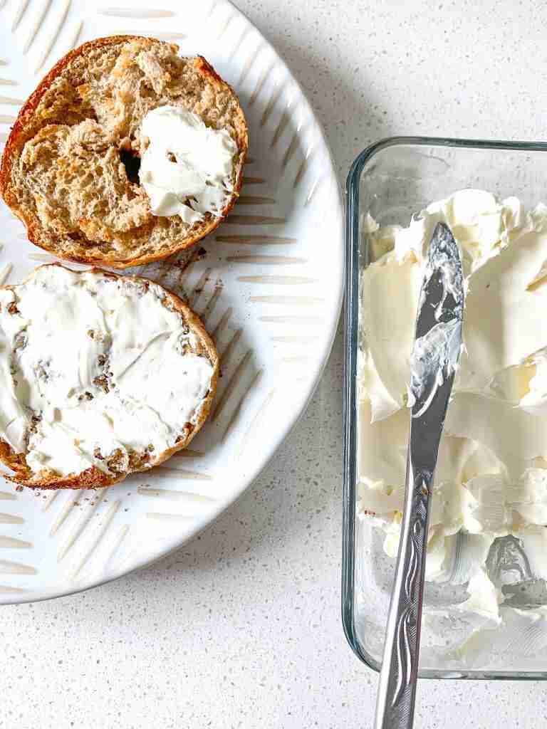 bagel cut in half getting spread with cream cheese