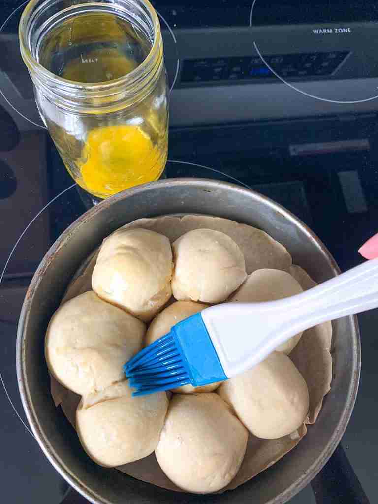 freshly baked sourdough dinner rolls being brushed with honey butter