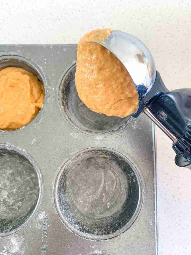 sourdough pumpkin batter being scooped into a muffin tin