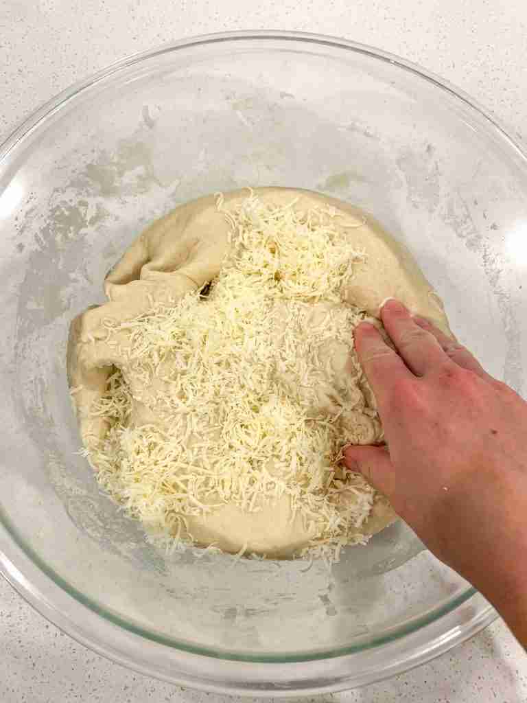mixing shredded asiago cheese into fermented dough