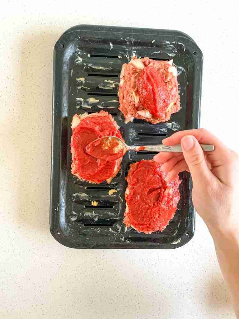 spreading homemade ketchup sauce on top of mini meatloaves before baking
