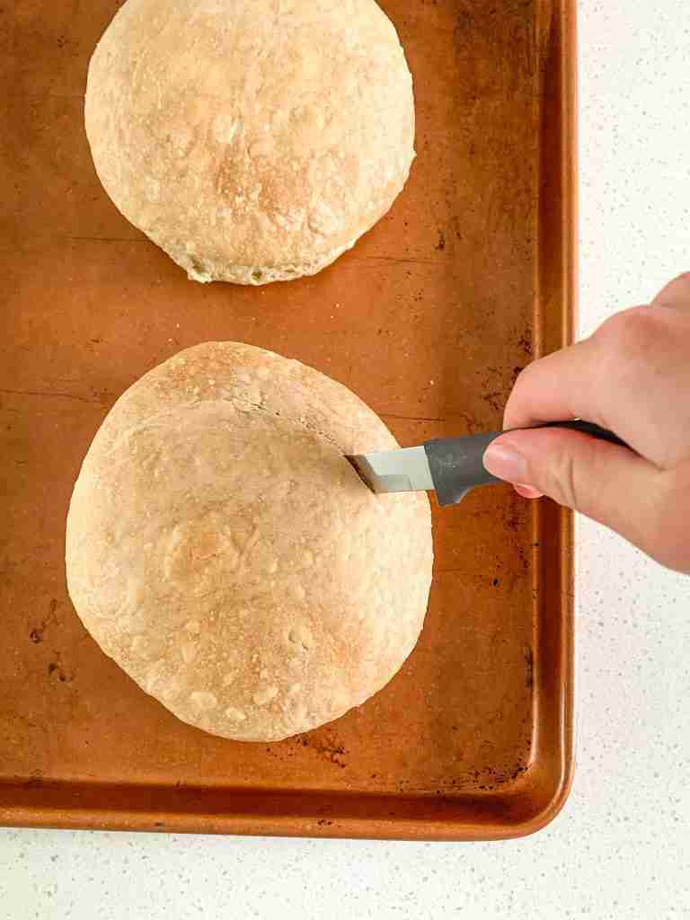 freshly baked sourdough bread bowl getting sliced to hollow out the center