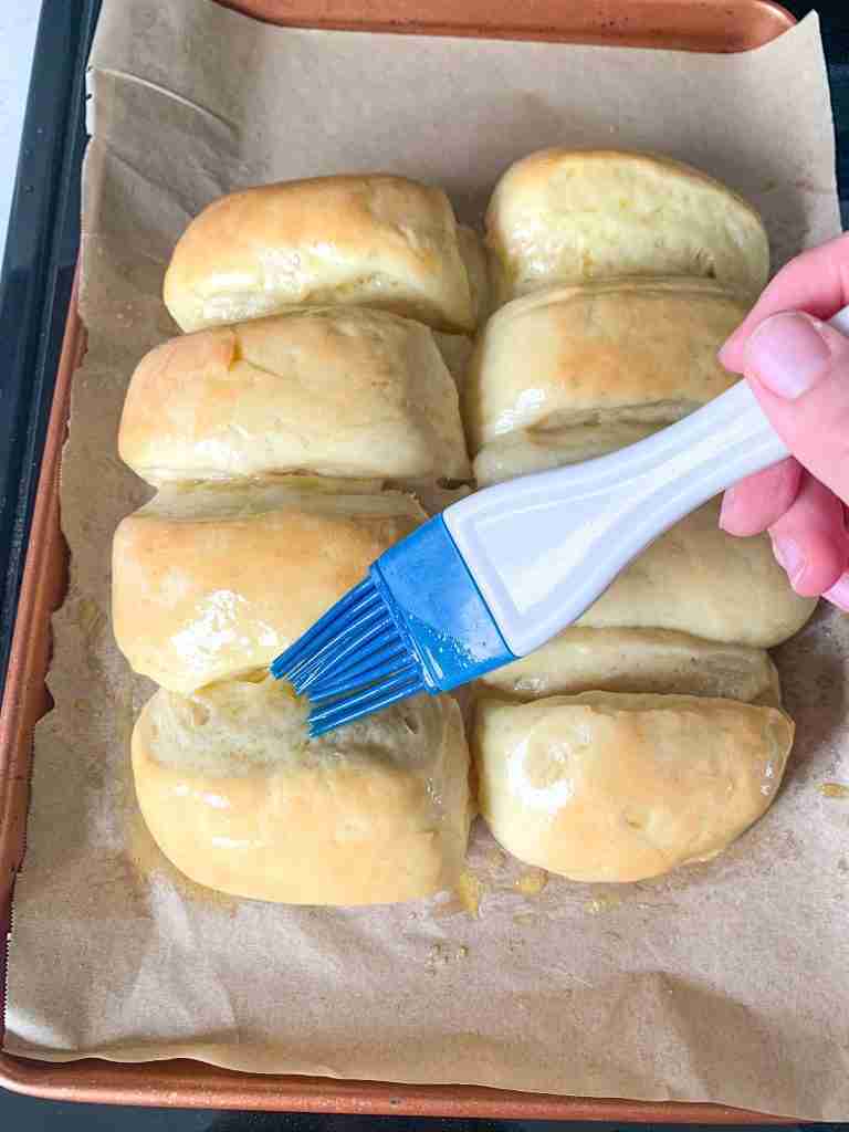 brushing butter on freshly baked sourdough parker house rolls