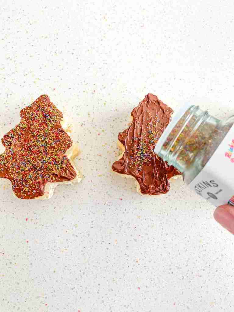 adding sprinkles for decoration on the sourdough little debbie christmas tree cakes