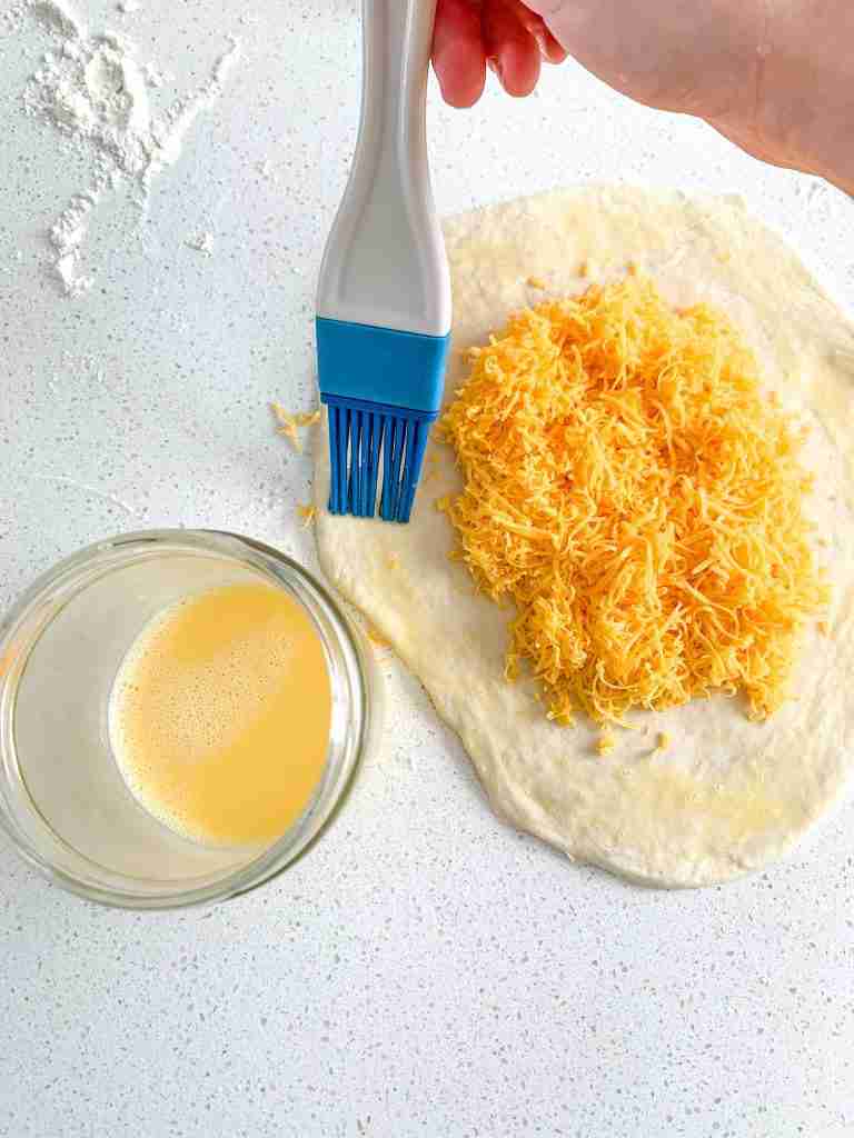 brushing the edges of a calzone dough filled with cheese before sealing