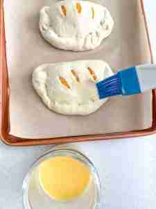 brushing shaped calzones with egg wash before baking