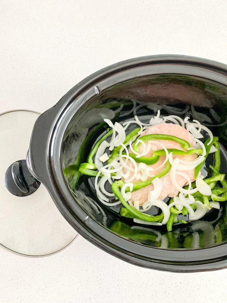 onion, chicken, and peppers in a slow cooker ready to cook